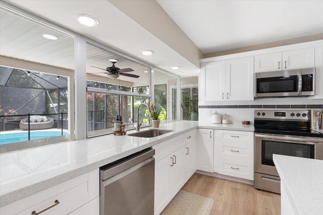 kitchen featuring sink, stainless steel appliances, light hardwood / wood-style floors, light stone countertops, and white cabinets