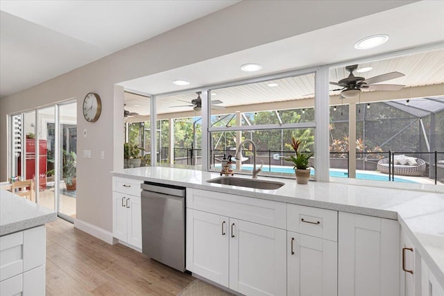 kitchen with white cabinetry, sink, stainless steel dishwasher, and light stone countertops