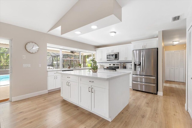 kitchen with white cabinetry, appliances with stainless steel finishes, a kitchen island, and light hardwood / wood-style flooring