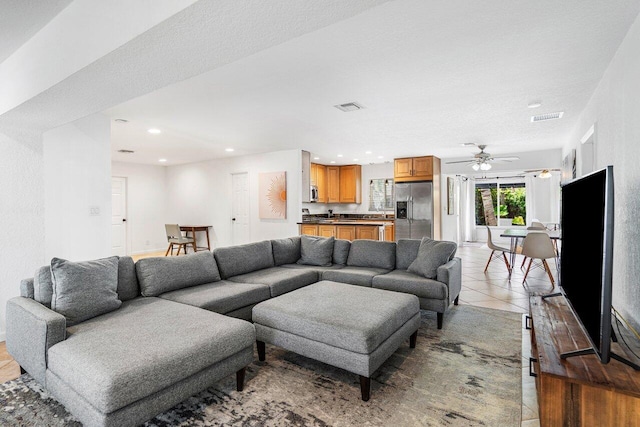 living room with ceiling fan, light tile patterned flooring, and a textured ceiling