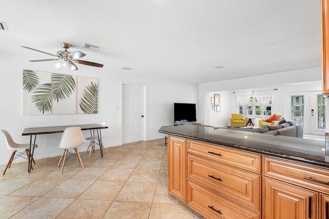 kitchen with light tile patterned flooring, dark stone counters, a textured ceiling, and ceiling fan