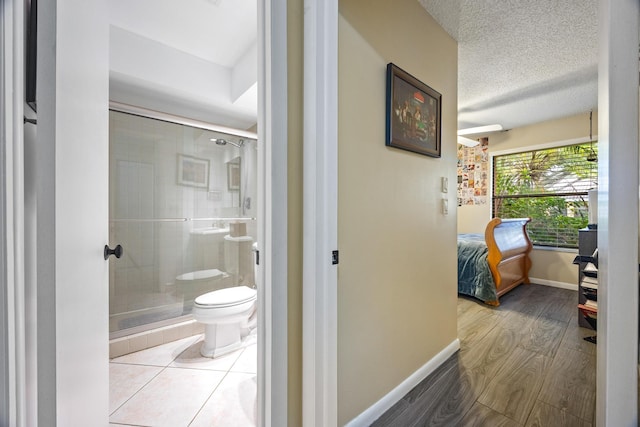 bathroom featuring wood-type flooring, a textured ceiling, toilet, and a shower with door