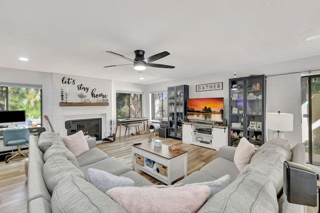 living room with light wood-type flooring, a large fireplace, and ceiling fan