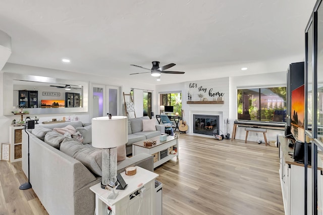 living room featuring light wood-type flooring, a fireplace, and ceiling fan