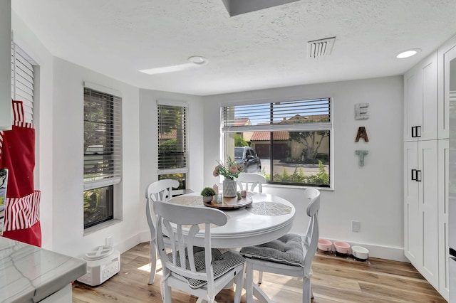 dining space with light wood-type flooring and a textured ceiling