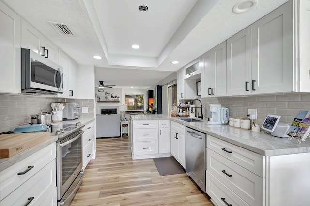 kitchen with ceiling fan, white cabinets, sink, kitchen peninsula, and stainless steel appliances