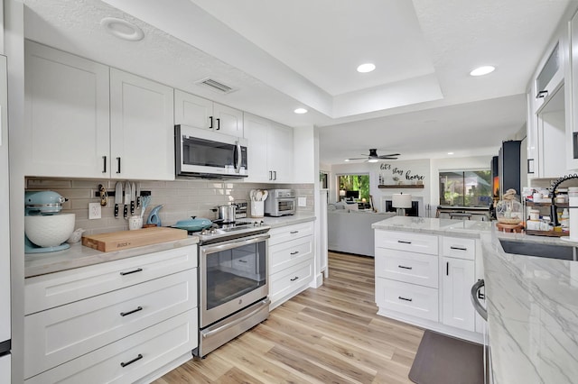 kitchen with sink, white cabinets, light hardwood / wood-style flooring, stainless steel appliances, and ceiling fan