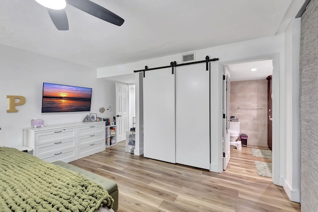 bedroom with tile walls, a barn door, connected bathroom, light wood-type flooring, and ceiling fan