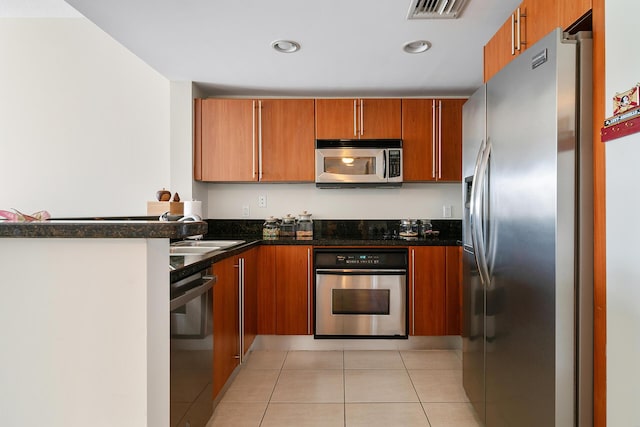 kitchen featuring stainless steel appliances, sink, light tile patterned floors, and dark stone counters