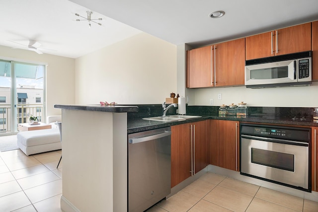 kitchen featuring sink, dark stone countertops, light tile patterned floors, kitchen peninsula, and stainless steel appliances