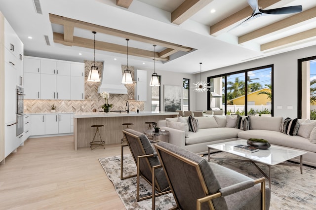 living room featuring ceiling fan, a raised ceiling, beamed ceiling, light hardwood / wood-style floors, and sink