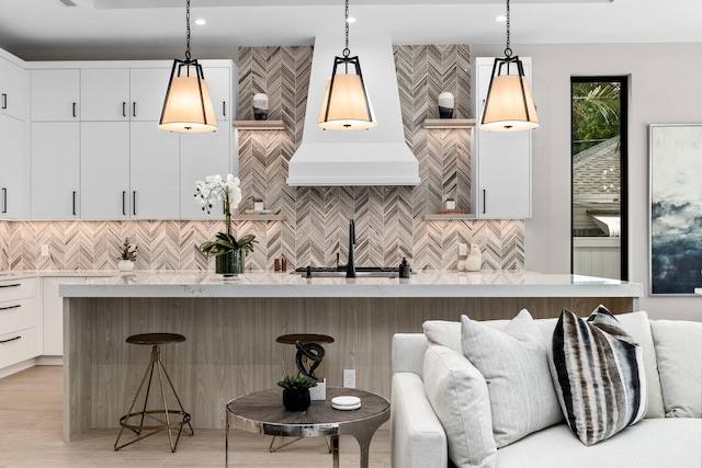 kitchen featuring a center island with sink, hanging light fixtures, a kitchen breakfast bar, white cabinetry, and light wood-type flooring