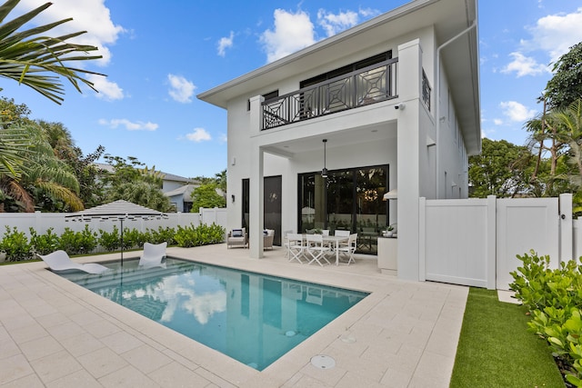 rear view of property with a patio, a fenced in pool, and a balcony