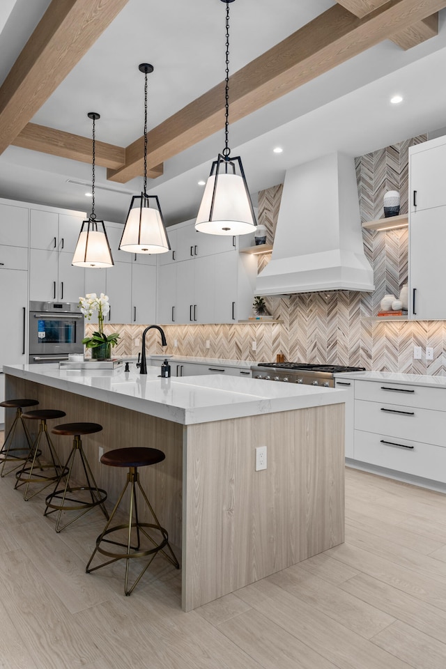 kitchen featuring a large island with sink, custom exhaust hood, and white cabinets