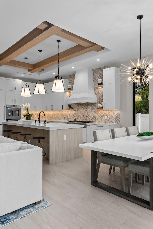 kitchen with a spacious island, a tray ceiling, decorative light fixtures, white cabinets, and premium range hood