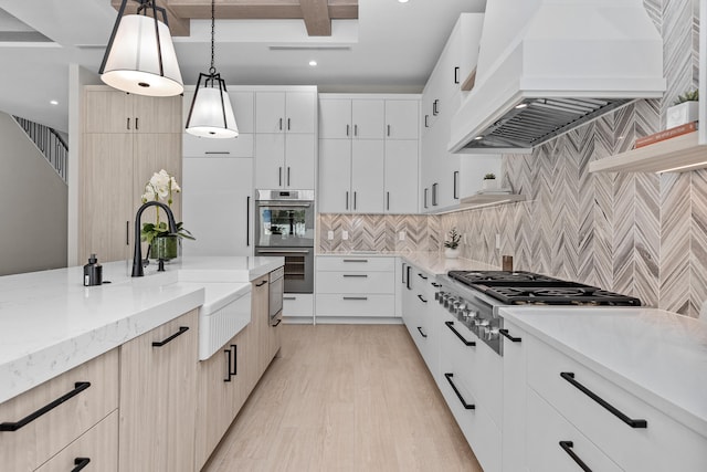 kitchen with light stone countertops, light wood-type flooring, hanging light fixtures, white cabinetry, and premium range hood