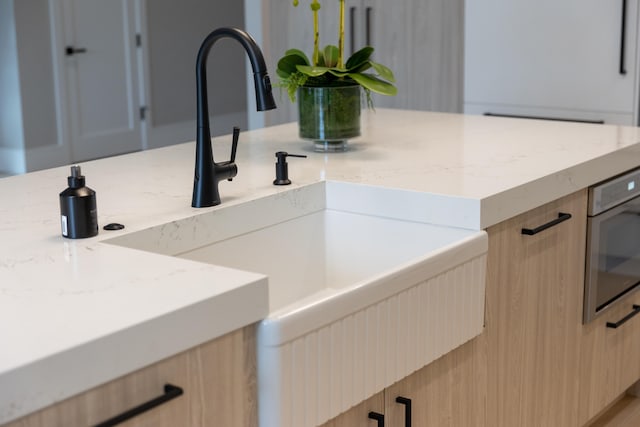 room details with light stone countertops, sink, light brown cabinets, and stainless steel oven