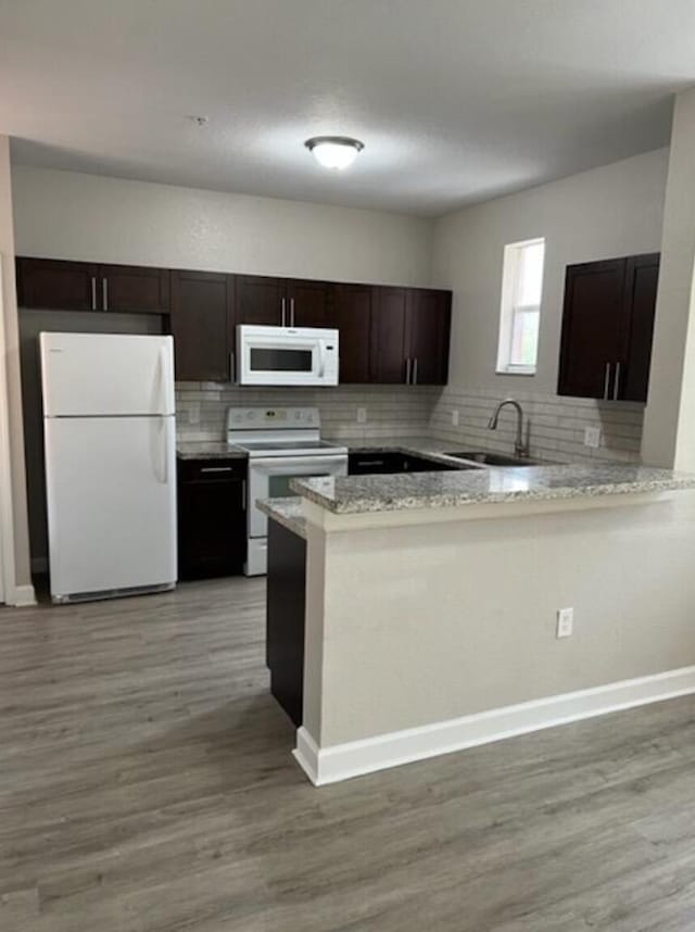 kitchen featuring light stone counters, white appliances, kitchen peninsula, light hardwood / wood-style flooring, and sink