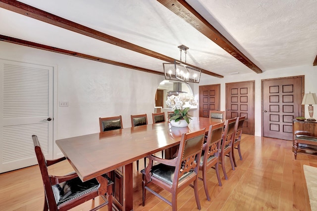 dining room with beamed ceiling, a textured ceiling, light wood-type flooring, and an inviting chandelier