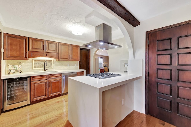 kitchen with appliances with stainless steel finishes, island range hood, beverage cooler, sink, and light hardwood / wood-style flooring