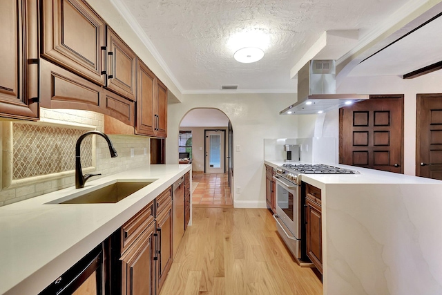 kitchen featuring sink, high end stove, extractor fan, light hardwood / wood-style floors, and a textured ceiling