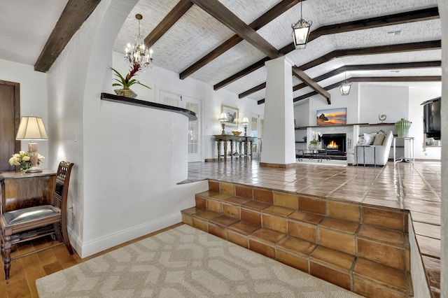 living room featuring a notable chandelier, vaulted ceiling with beams, wood-type flooring, and a tiled fireplace