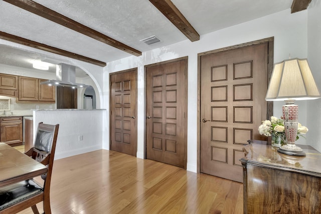 entryway with beamed ceiling, a textured ceiling, and light hardwood / wood-style floors