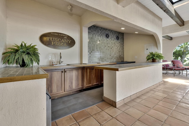 bar with beamed ceiling, light tile patterned floors, sink, and tile countertops