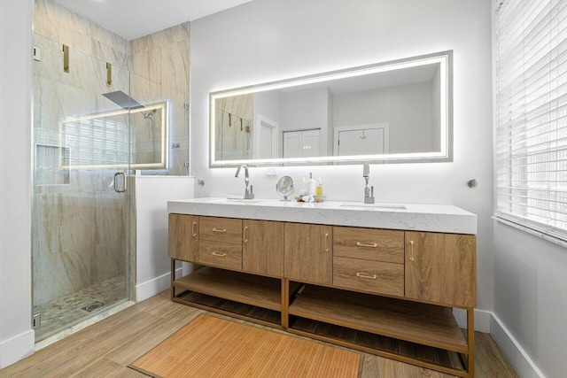 bathroom featuring a sink, wood finished floors, a stall shower, double vanity, and baseboards