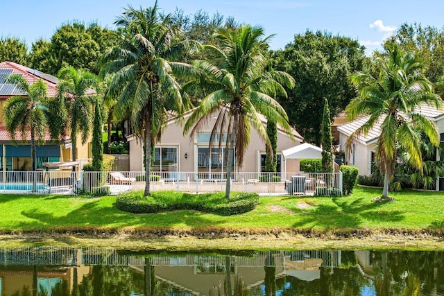 back of house featuring fence, a water view, stucco siding, and a lawn