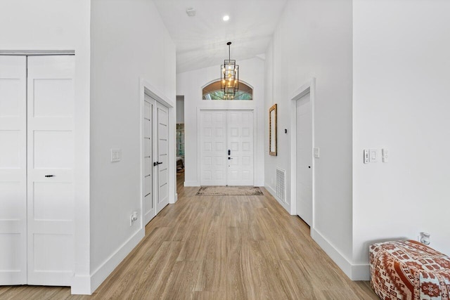 foyer entrance with light wood-type flooring, high vaulted ceiling, and an inviting chandelier