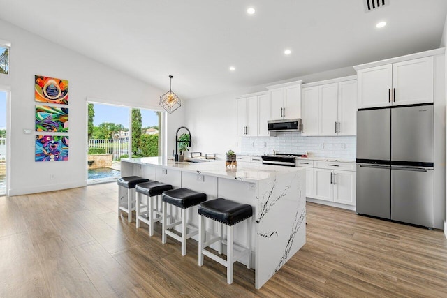 kitchen with a sink, stainless steel appliances, tasteful backsplash, a kitchen island with sink, and light wood finished floors