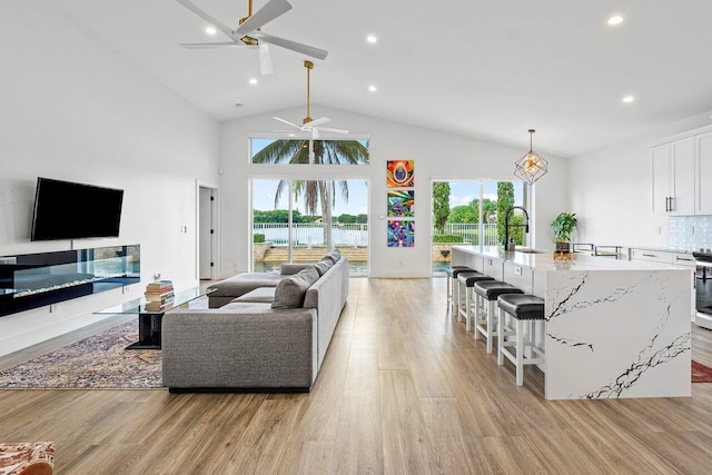 living area with light wood-type flooring, high vaulted ceiling, a ceiling fan, and recessed lighting