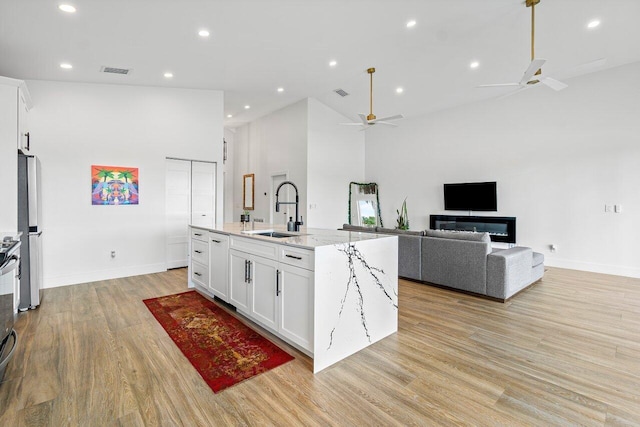 kitchen with a sink, high vaulted ceiling, light wood finished floors, a ceiling fan, and white cabinets