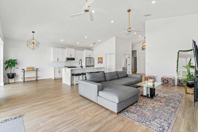 living room with high vaulted ceiling, ceiling fan, sink, and light hardwood / wood-style floors