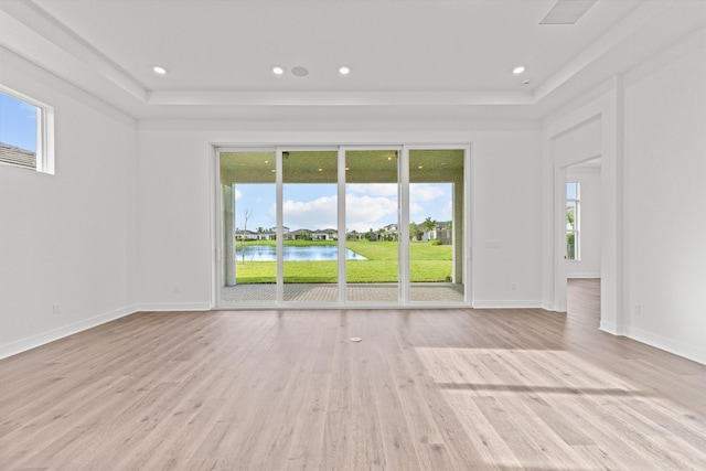 spare room with a tray ceiling, a water view, and light wood-type flooring