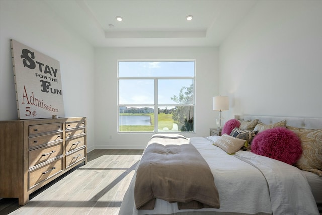 bedroom with a tray ceiling, light hardwood / wood-style flooring, and a water view