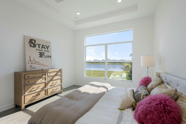 bedroom featuring a raised ceiling, a water view, and hardwood / wood-style flooring