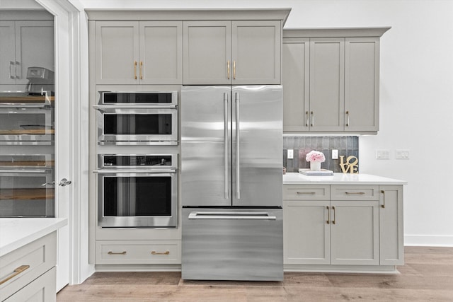 kitchen with backsplash, gray cabinets, stainless steel appliances, and light hardwood / wood-style floors