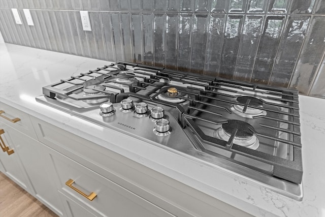 interior details featuring stainless steel gas stovetop, light stone countertops, light wood-type flooring, tasteful backsplash, and white cabinetry