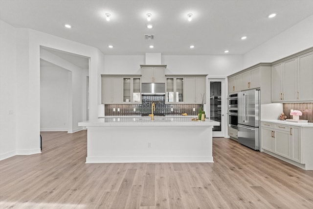 kitchen with tasteful backsplash, stainless steel appliances, light hardwood / wood-style flooring, gray cabinets, and an island with sink