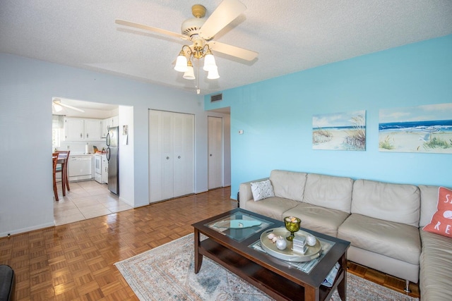 living room with ceiling fan, light parquet floors, and a textured ceiling