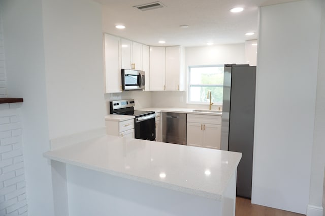 kitchen with light stone countertops, white cabinets, kitchen peninsula, and stainless steel appliances