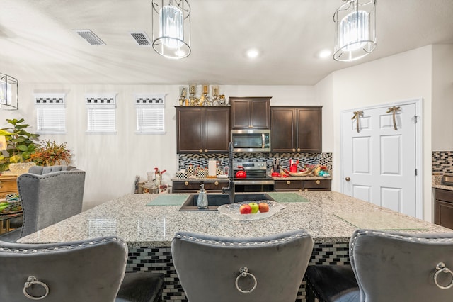 kitchen with an island with sink, stainless steel appliances, dark brown cabinets, and pendant lighting