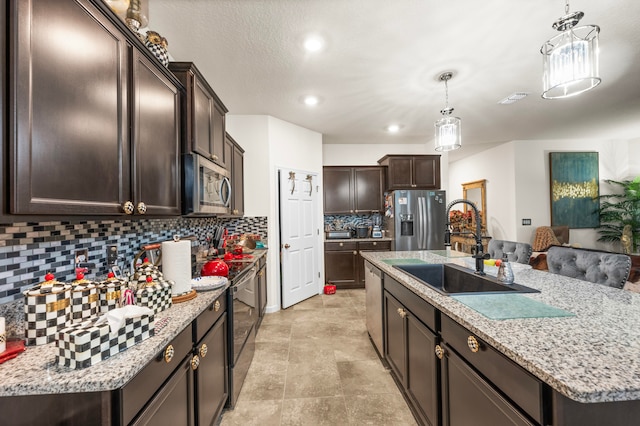 kitchen featuring sink, backsplash, stainless steel appliances, decorative light fixtures, and a center island with sink