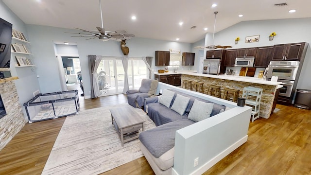 living room featuring a stone fireplace, lofted ceiling, light wood-type flooring, and ceiling fan