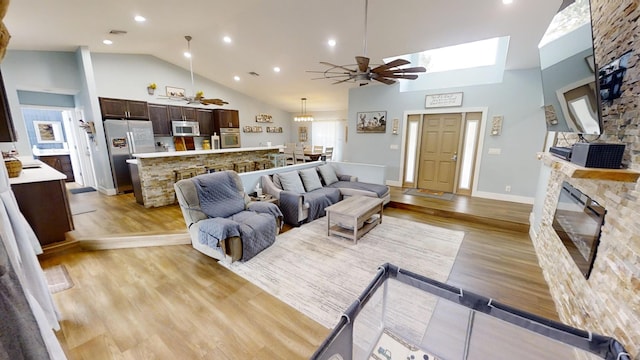 living room with high vaulted ceiling, a fireplace, ceiling fan, and light hardwood / wood-style flooring