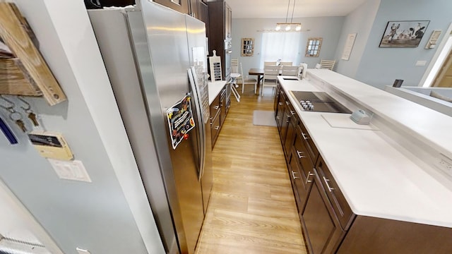 kitchen featuring stainless steel fridge, pendant lighting, light wood-type flooring, black electric stovetop, and a chandelier