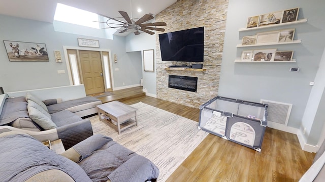 living room with ceiling fan, a stone fireplace, hardwood / wood-style floors, and high vaulted ceiling