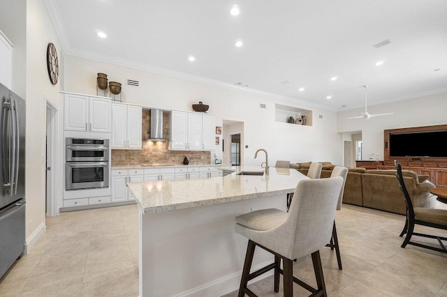 kitchen featuring stainless steel appliances, white cabinets, sink, wall chimney range hood, and light stone countertops